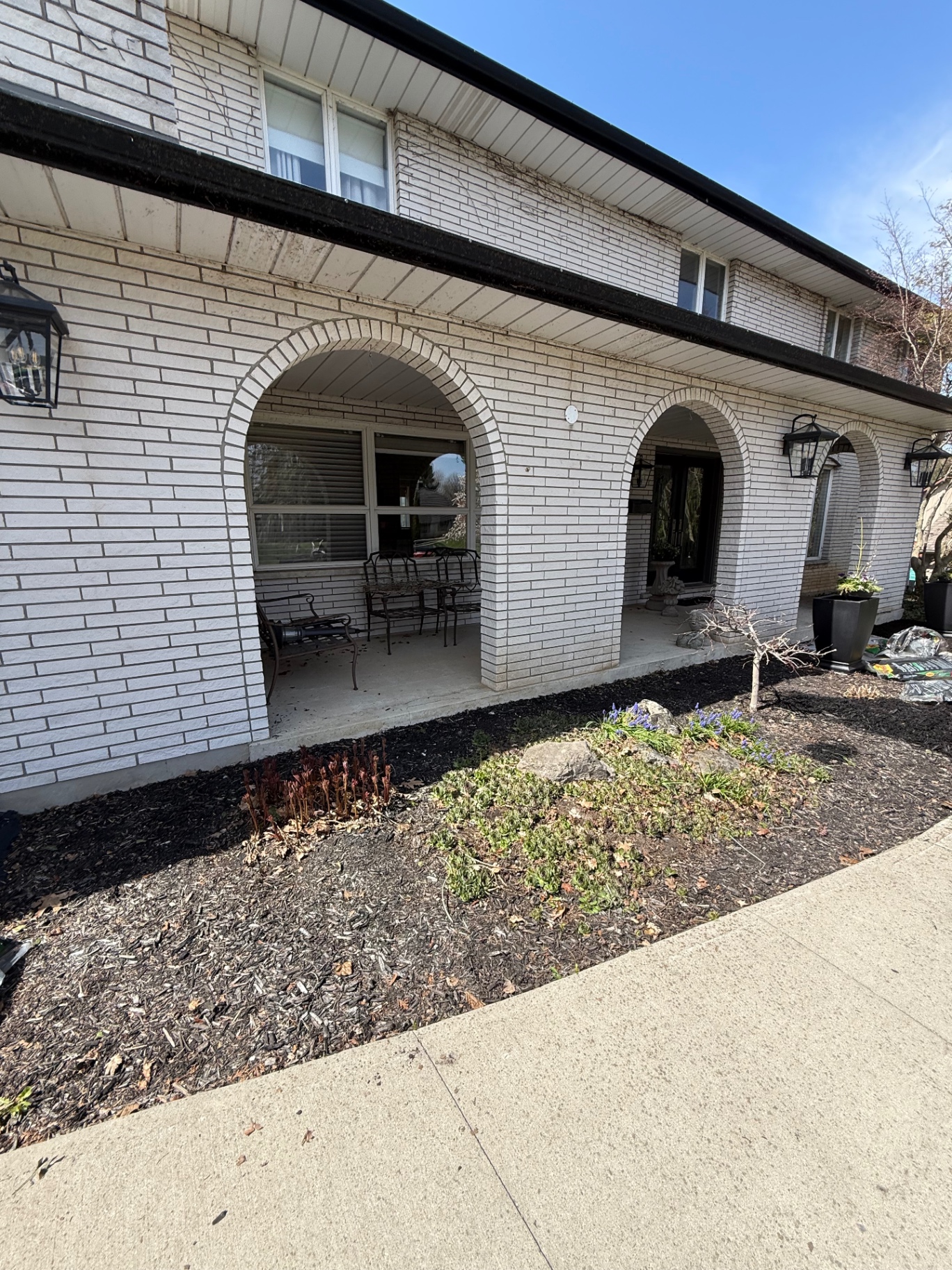 Before — Front entrance landscape construction in Ancaster — tired garden bed cleaned up, edged, and finished with fresh black mulch along the arched portico