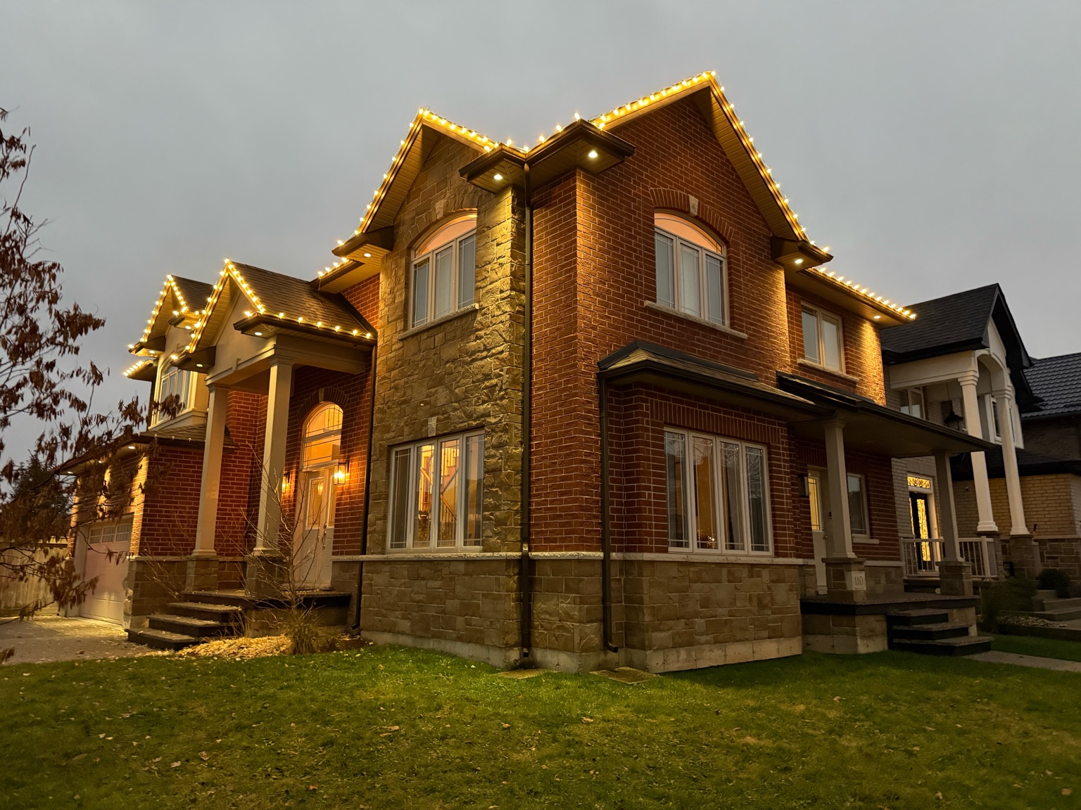 Warm white holiday roofline lights installed on a corner-lot home