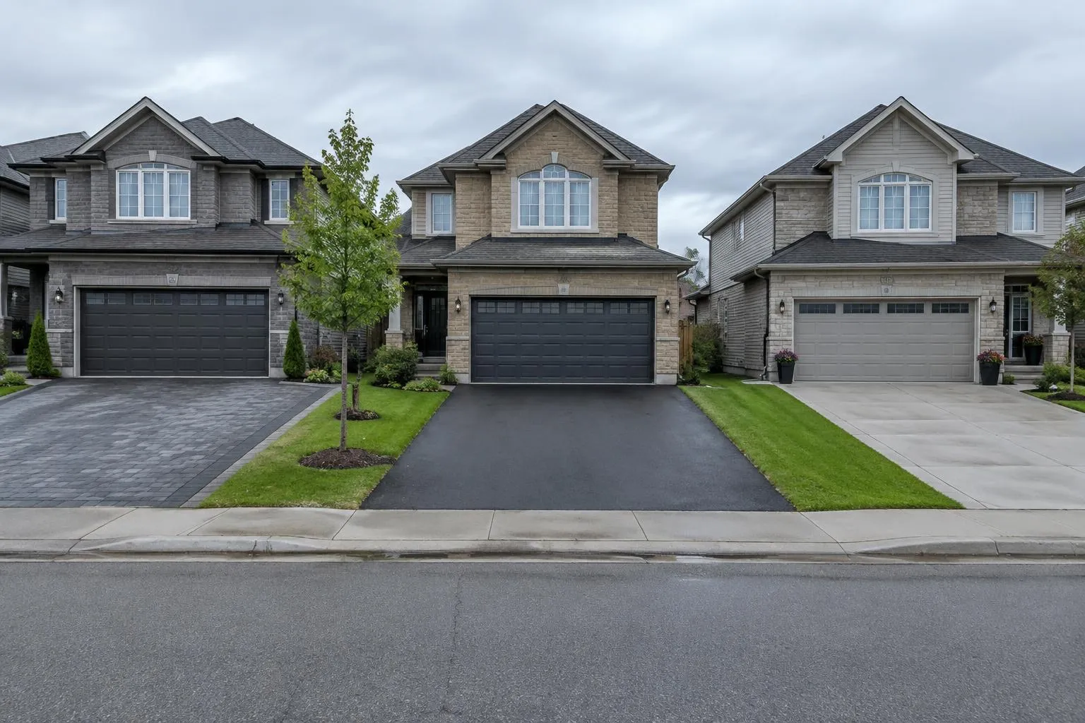 Three neighbouring suburban homes with an interlock driveway, a black asphalt driveway and a light grey concrete driveway side by side