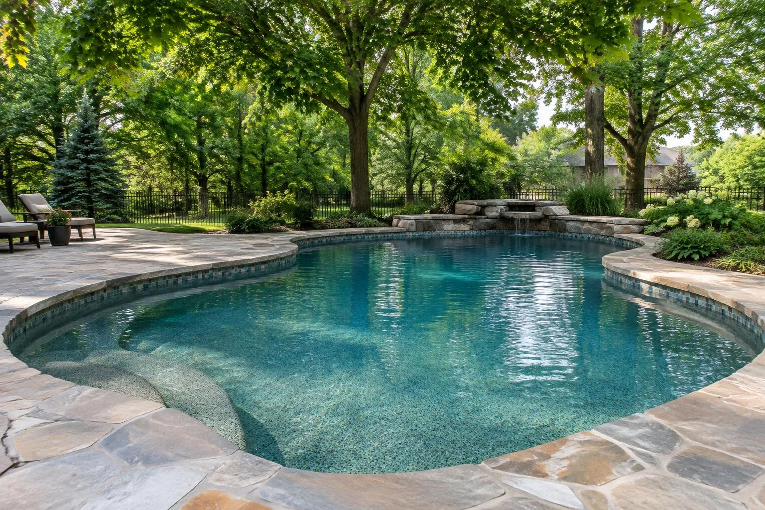 Freeform concrete pool with waterline tile and natural stone coping under mature maples