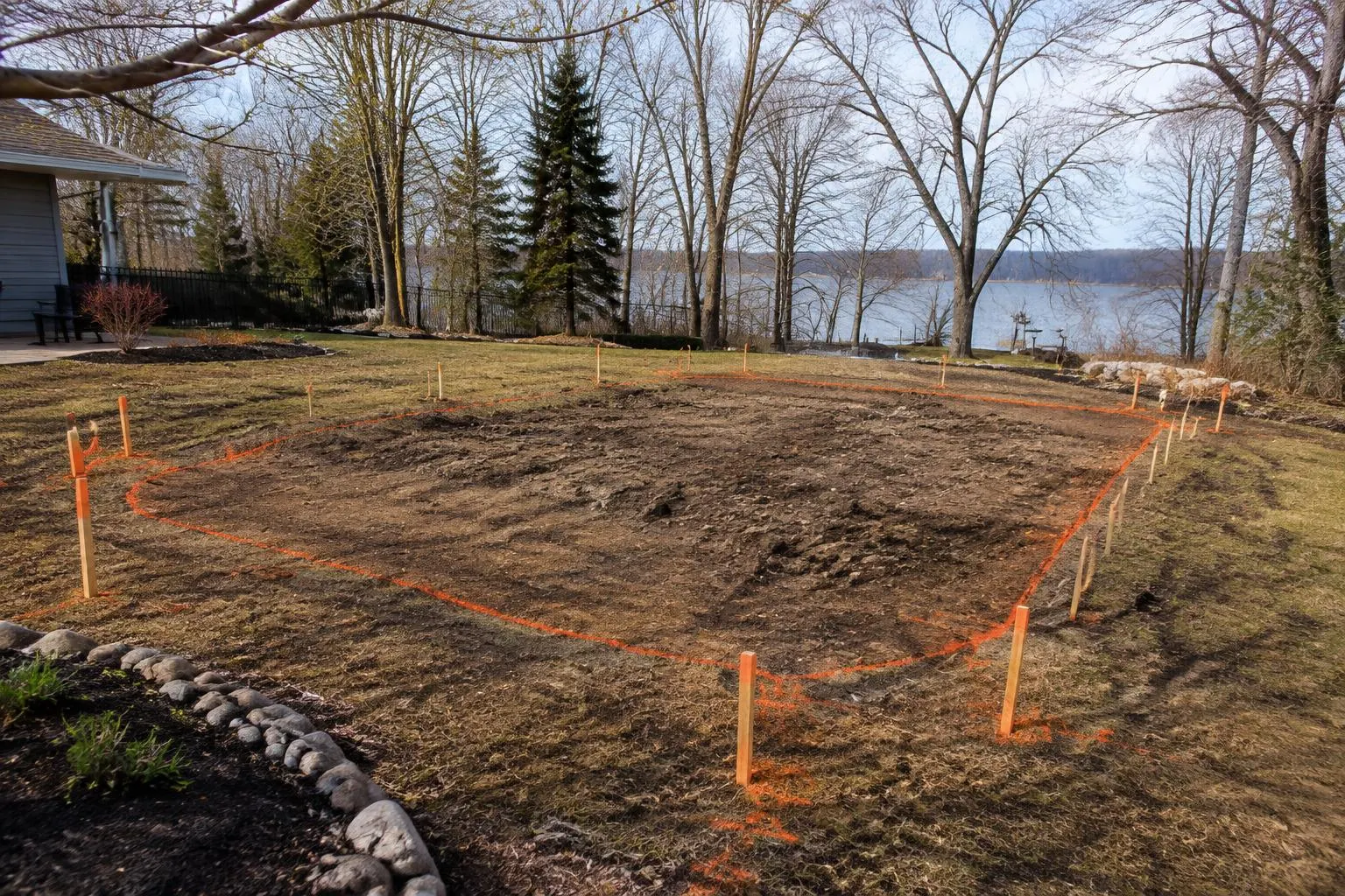 Thawed spring backyard with survey stakes and orange paint outlining a future pool